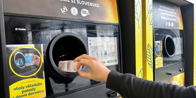 Ruka vkládá PET lahev do stroje na vratné lahve.