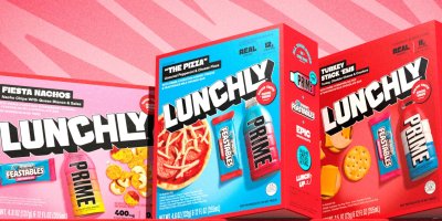 Tři krabičky s různými obědovými jídly, jako je pizza, nachos nebo sendviče, sladkostí a nápojem Prime.