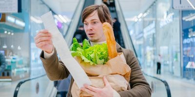 Muž si se zděšením prohlíží účtenku od nákupu.