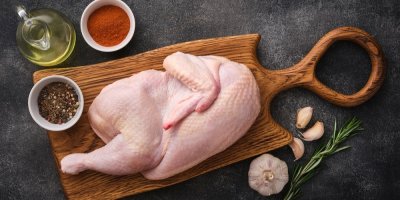 Polovina syrového kuřete na prkénku, okolo ingredience na vaření