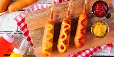Tři corn dogy s hořčicí a kečupem na dřevěném prkénku