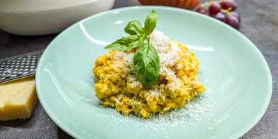 Dýňové rizoto na talíři posypané strouhaným sýrem a ozdobené bazalkou
