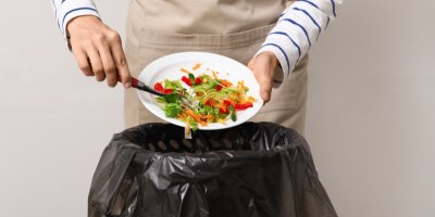 Člověk shrnuje zeleninové jídlo z talíře do odpadkového koše.