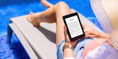 Žena si čte u vody na lehátku na čtečce knihu