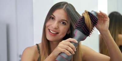 Žena si s úsměvem natáčí vlasy pomocí horkovzdušného kartáče.