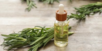 Lahvička rozmarýnového oleje, vedle je ní je položená snítka rozmarýnu