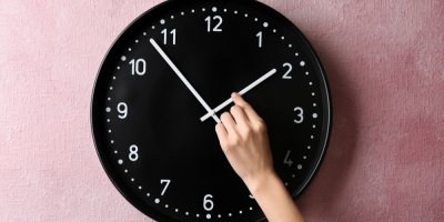 Ruka přetáčí ručičky na nástěnných hodinách.