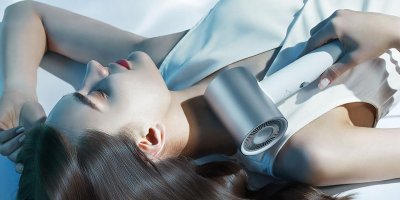 Ležící žena drží v rukou stříbrný vysoušeč vlasů Xiaomi Water Ionic Hair Dryer.