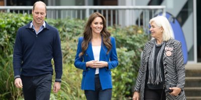 Princezna Kate ve vypasovaném modrém saku a džínech, po jejím boku její manžel a další žena