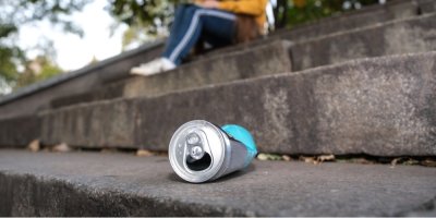 Plechovka leží na zemi, v pozadí sedí dívka