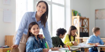 Děti sedící ve škole a usmívající se učitelka