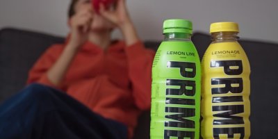 Dvě lahve s nápojem Prime a v pozadí chlapec, který pije z třetí.