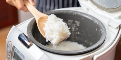 Člověk pomocí dřevěné vařečky vyndává uvařenou rýži z rýžovaru.