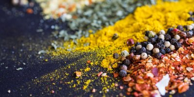 Různé druhy koření na černém podkladu – kurkuma, pepř, paprika a sušené bylinky