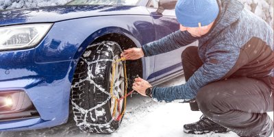 Muž nasazuje na pneumatiku zimní řetězy.