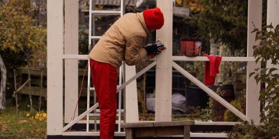 Muž nanáší impregnaci na dřevěnou stavbu na zahradě.