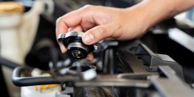 Ruka drží v ruce uzávěr na nádobu v motoru auta