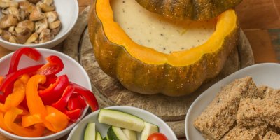 Rozpuštěný sýr v pečené dýni, okolo nakrájené kousky papriky, okurků, opečených žampionl a chléb