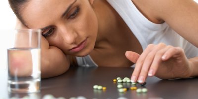 Žena sedí za stole se unaveně dívá na prášky