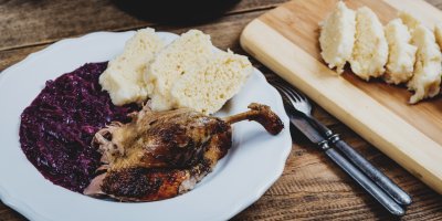 Kachní stehno na talíři s červeným zelím a nakrájeným houskovým knedlíkem