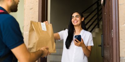 Žena přebírá balíček jídla od donáškové služby.