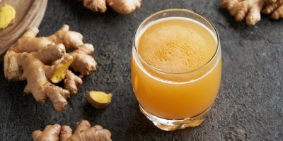 Žlutý nápoj ve skleničce, okolo kusy zázvoru