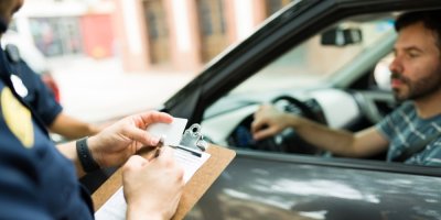 Policista vypisuje pokutu řidiči za volantem vozu.