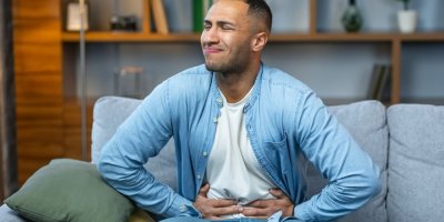 Muž sedí na gauči a drží se za břicho