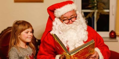 Muž v červeném kostýmu Santa Clause čte z velké knihy před malou holčičkou