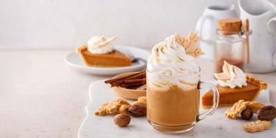 Šálek s mléčnou kávou s velkou porcí šlehačky, v pozadí kousky dortů