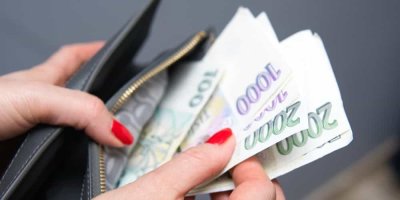 Žena s červeně nalakovanými nehty vkládá české bankovky do peněženky
