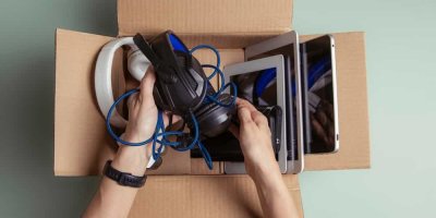 Člověk vkládá elektroniku (tablety a sluchátka) do kartonové krabice