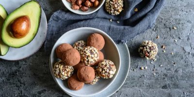 Miska plná čokoládovo-oříškových kuliček a vedle ní rozkrojené avokádo a miska lískových oříšků