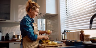 Žena škrábe brambory v kuchyni