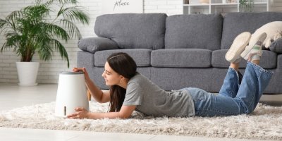 Mladá žena leží na koberci a prohlíží si zvlhčovač vzduchu