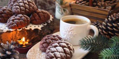 Kakaové cukroví ve tvaru šišek vedle hrníčku kávy, obklopené vánočními dekoracemi