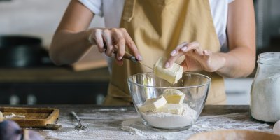 Žena přidává do mísy s moukou nakrájené máslo