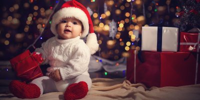 Batole sedí u stromečku, drží malý dárek a směje se