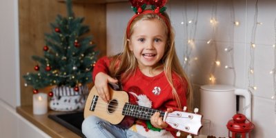 Malá holčička hraje na malou kytaru vedle vánočního stromku