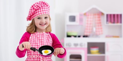 Dívka drží malou pánvičku před dětskou kuchyňkou