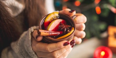 Žena drží šálek červeného svařeného vína, ve kterém je skořice, badyán, jablko a pomeranč