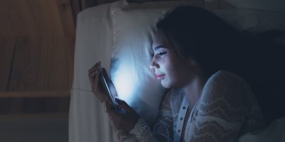 Žena leží v posteli a obličej jí ozařuje světlo z mobilu