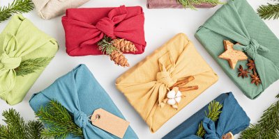 Několik dárků zabalených do různě barevných šátků a ozdobených větvičkami, šiškami, skořicí či badyánem