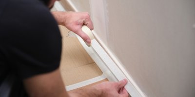 Člověk oblepuje podlahu maskovací páskou před malováním 