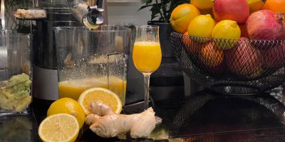 Sklenice z džusem, okolo odšťavňovač, ovoce a zázvor