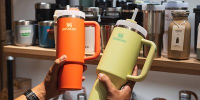 Člověk drží oranžový a žlutý hrnek Stanley