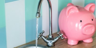 Voda tekoucí z kohoutku a kasička na peníze v podobě prasátka