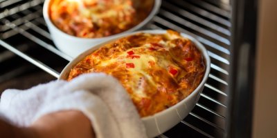 Člověk vytahuje z trouby keramickou mísu s jídlem, druhá v troubě ještě zůstává.