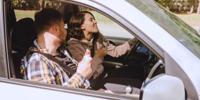 Mladý muž a žena za volantem jedí čokoládové tyčinky a usmívají se