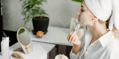 Žena s ručníkovým turbanem na hlavě si nanáší peeling na pleť.